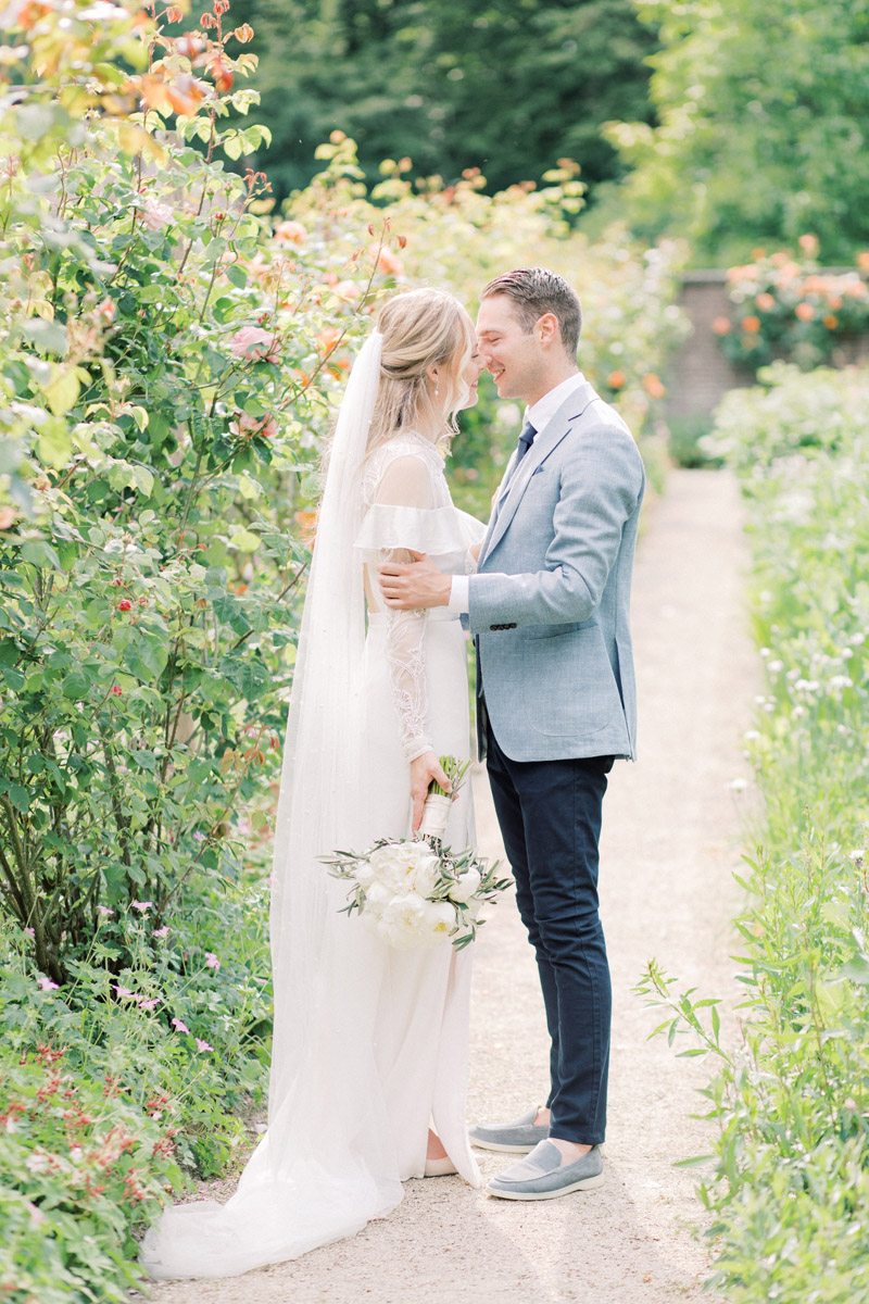 Fine art bruidsfotograaf Milou van Ham Fotografie intieme buiten bruiloft bij trouwlocatie Tuin de Lage Oorsprong in Oosterbeek en hotel de Bilderberg kleine romantische bruiloft lichte romantische trouwfoto's trouwfotograaf trouwen in een kas Nederland Belgie Amsterdam Dutch wedding photographer light and airy Europa destination wedding buiten trouwen met bruidsmeisjes wit bruidsboeket bruid tussen bloemen